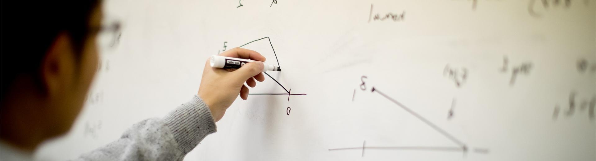 Temple student working out a math equation on a white board.
