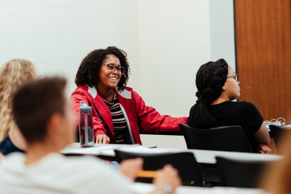 A female student in a red jacket smiles during a class discussion.